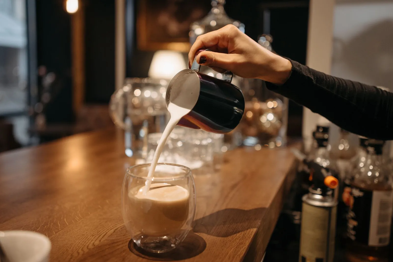 A barista pouring milk into coffee, creating a latte art in a cozy café setting.