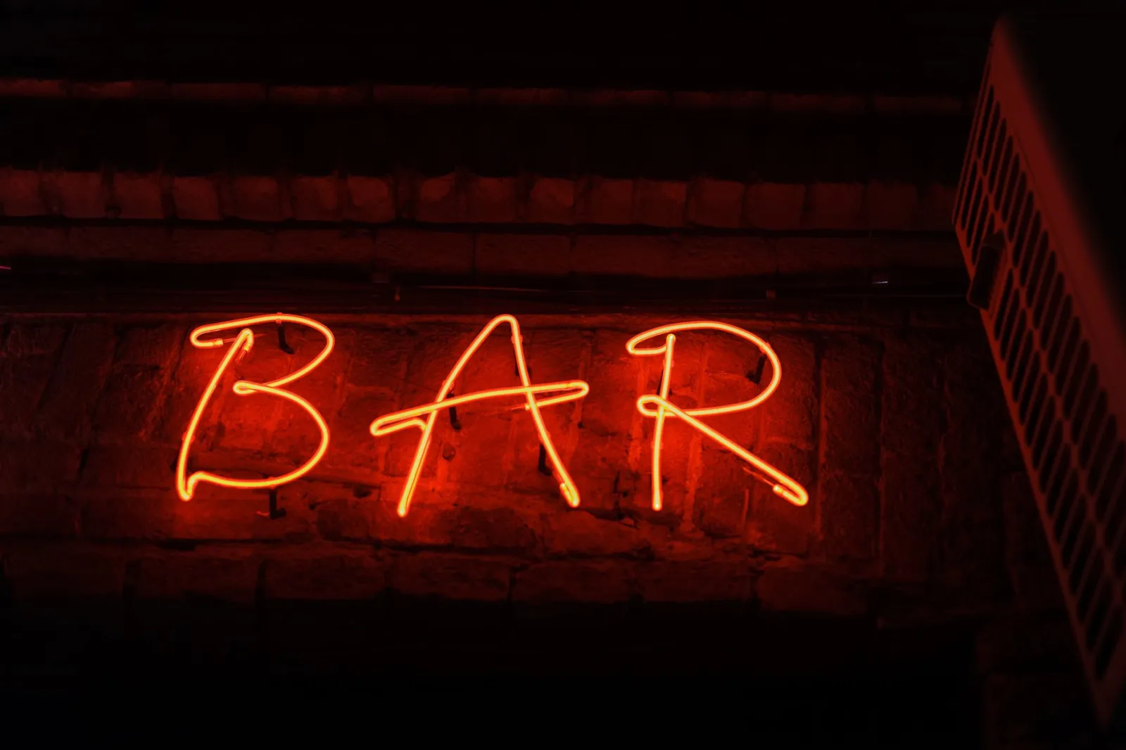 Bright neon sign spelling 'BAR' glowing against a dark brick wall, creating a vibrant nightlife atmosphere.