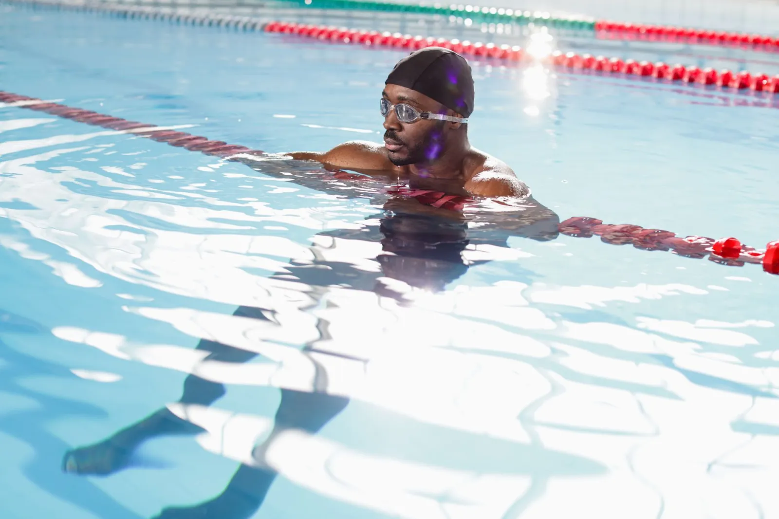 A focused swimmer wearing goggles and a swim cap in an indoor pool, perfecting his technique.