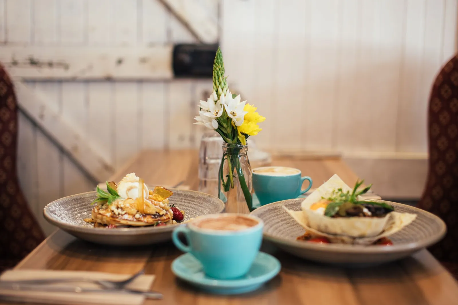 Table with cups of coffee and delicious pancakes with syrup salad in a bread plate in cafe in morning time