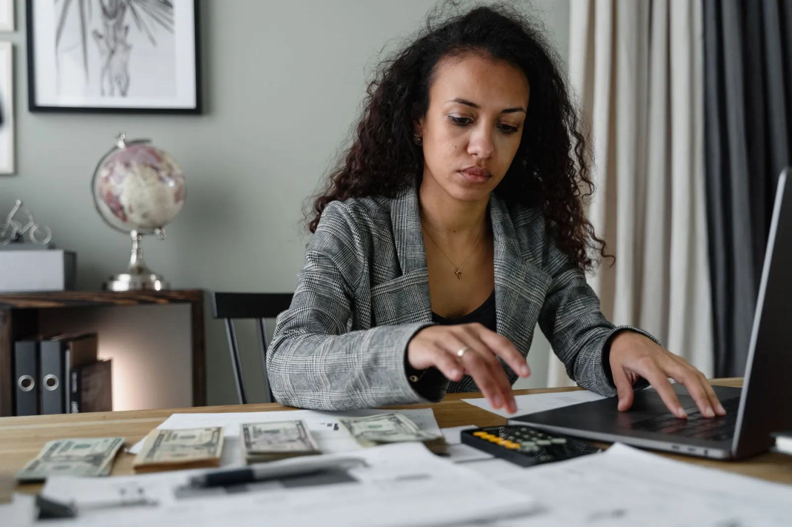 Professional woman analyzing financial documents and counting cash at office desk.